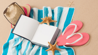 Book, beach towel, flip flops, and hat laying on a beach