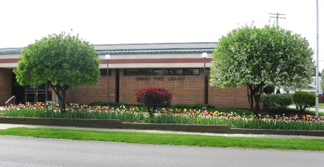 View of the library from the street with tree, shrub, and tulips in bloom