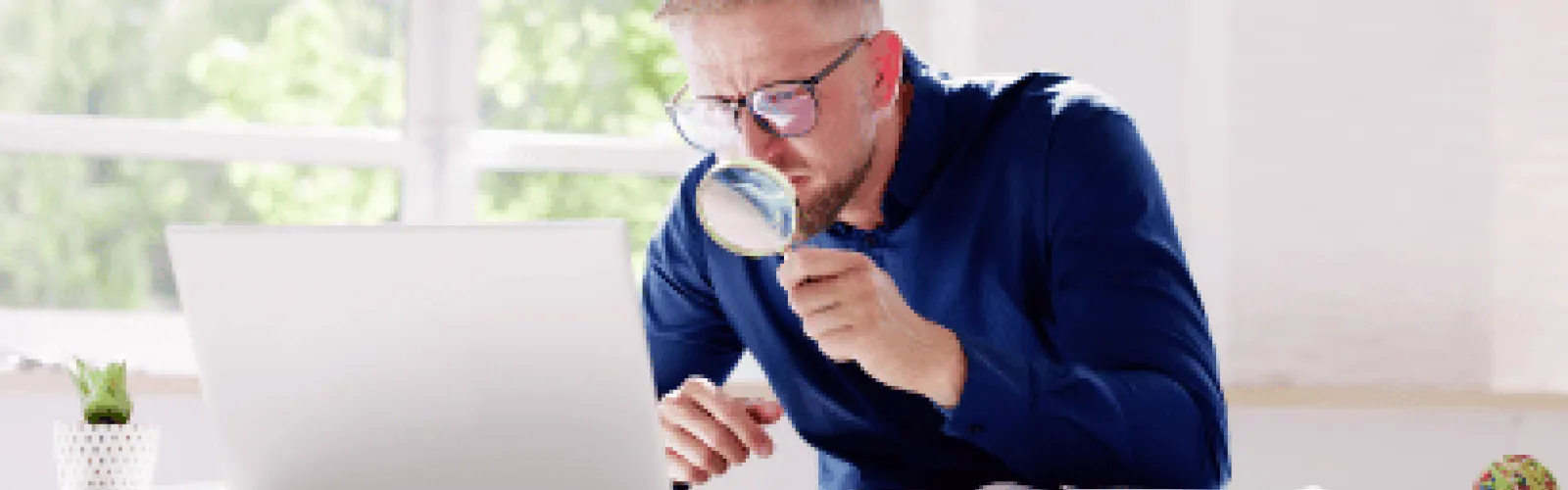 Man holding a magnifying glass in front of computer screen